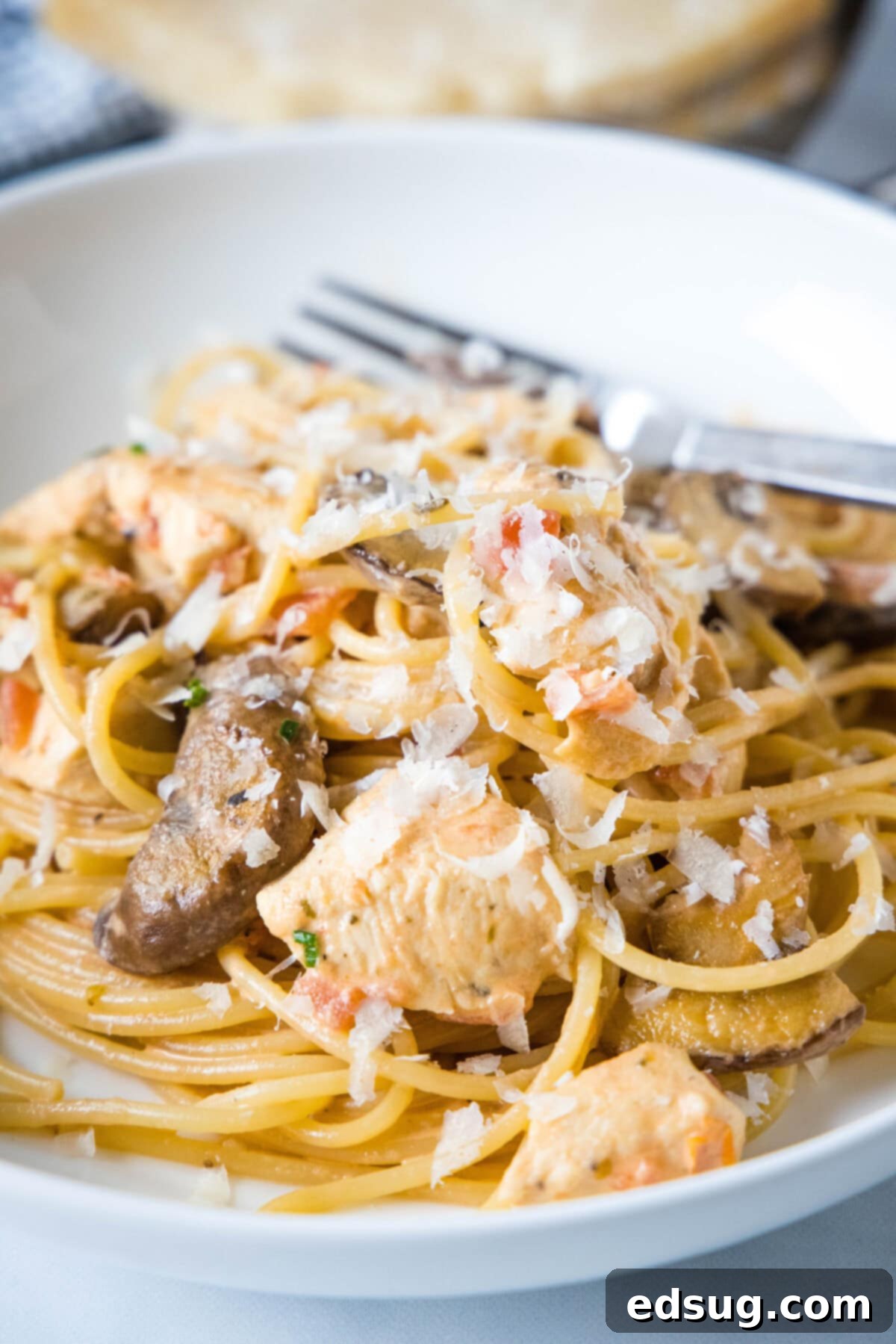 Creamy Tuscan Chicken Pasta 7 A generous serving of creamy Tuscan chicken pasta in a white bowl, garnished with fresh basil and grated Parmesan, showcasing the rich sauce and tender ingredients.