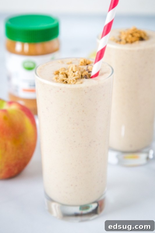 A tall glass of apple cinnamon smoothie, garnished with a sprinkle of granola and an apple slice, with a straw, set against a rustic wooden background.