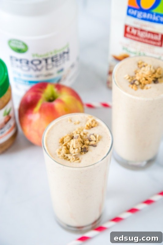 Various apple smoothie ingredients: a glass, almond milk, diced apple, protein powder, and almond butter, neatly arranged on a counter.