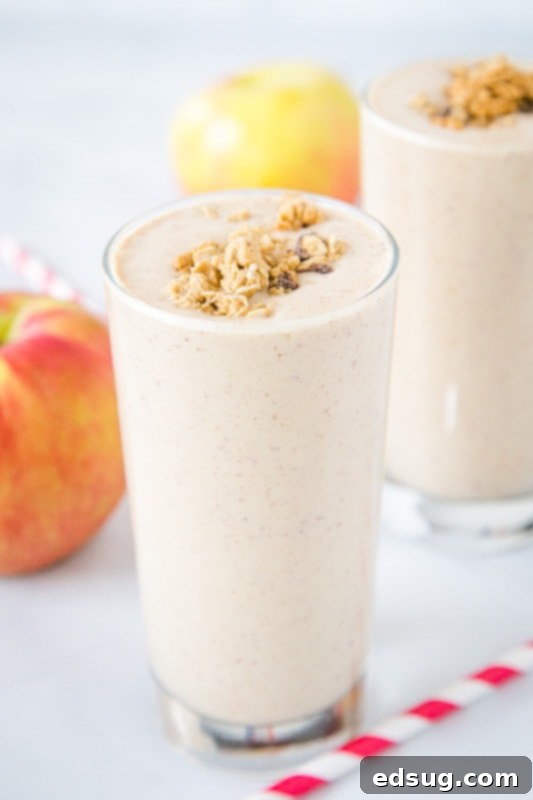 A beautifully textured apple smoothie in a glass, placed on a light wooden table, perfectly capturing a cozy autumn vibe.