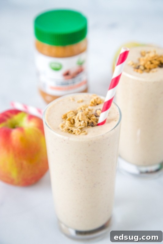 A refreshing apple cinnamon smoothie in a tall glass with a straw, garnished with a light sprinkle of cinnamon on top.
