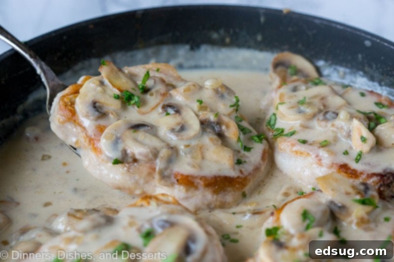 Smothered pork chops are a comforting one-pan recipe with juicy, pan-seared chops drenched in a creamy mushroom gravy. Quick and delicious! Close up of a spatula sliding under smothered pork chops with mushroom gravy in a skillet.