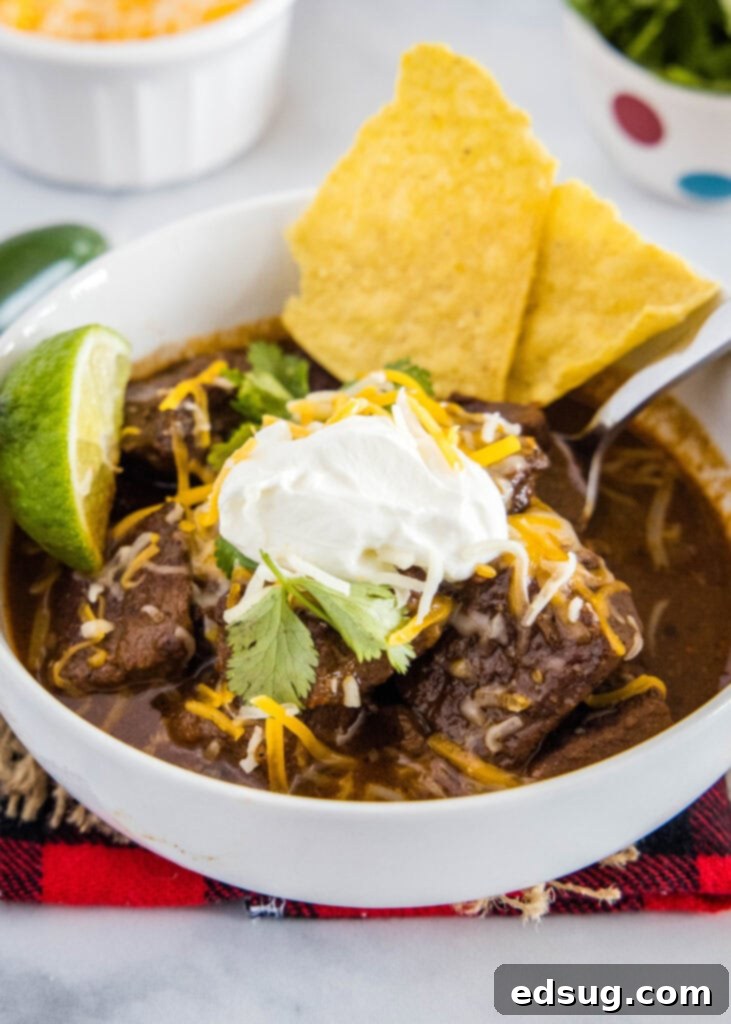Authentic Texas Chili 2 A bowl of rich Texas beef chili topped with fresh sour cream, shredded cheddar cheese, and crispy tortilla chips, ready to be enjoyed.