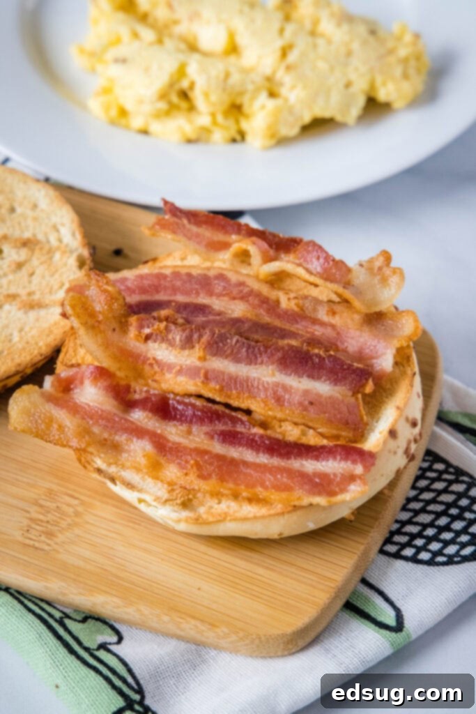 This classic bacon egg and cheese sandwich is the ultimate breakfast, with fluffy eggs, melty cheese, crispy bacon, and a toasted bagel. A bagel with strips of bacon on it, next to a plate of eggs