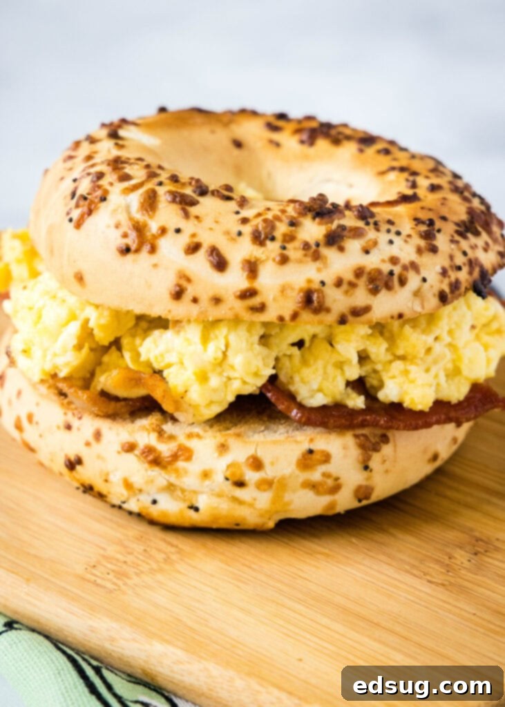 This classic bacon egg and cheese sandwich is the ultimate breakfast, with fluffy eggs, melty cheese, crispy bacon, and a toasted bagel. Close up of a bacon and egg bagel sandwich on a cutting board