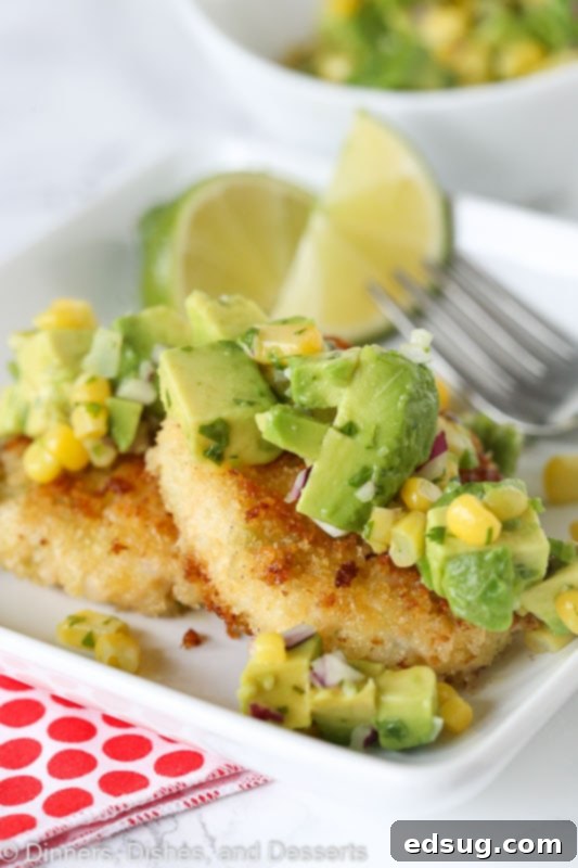 Golden brown shrimp cakes topped generously with fresh corn and avocado salsa, resting on a white plate, ready to be served.