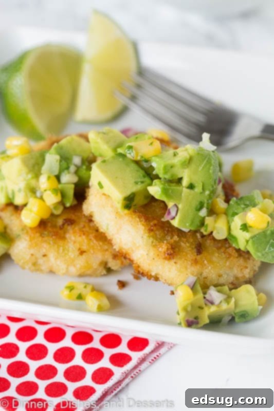 Close-up of a perfectly cooked shrimp cake, golden brown, with a fork digging into the fresh corn and avocado salsa on top.
