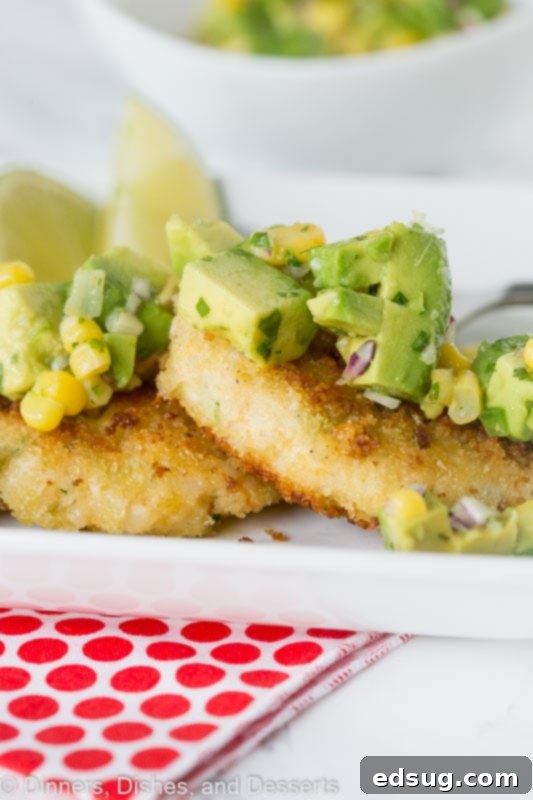 Three golden-brown shrimp cakes artfully arranged on a plate, each adorned with a generous dollop of fresh corn and avocado salsa, garnished with cilantro.