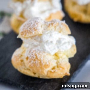 Close up of a cream puff dusted with powdered sugar on a platter with more cream puffs in the background.
