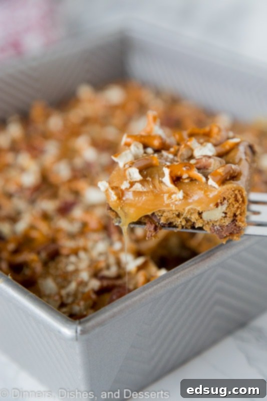 A close-up of a single Butter Pecan Pretzel Bar, rich with caramel and pecans, placed beside the baking pan.