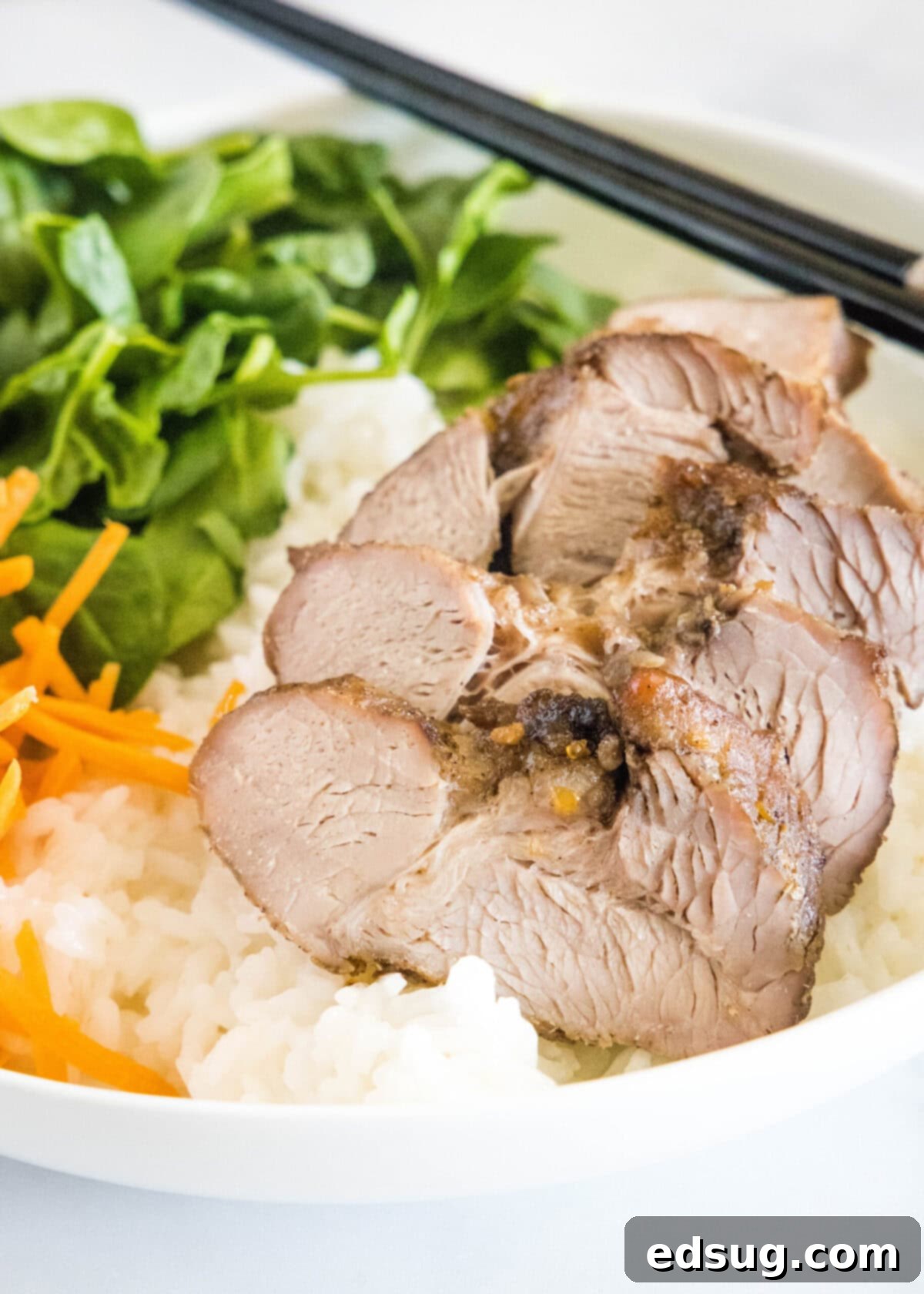 This easy char siu pork recipe is tender, juicy, and loaded with your favorite Chinese flavors like hoisin and five-spice powder.  Close up of char siu pork in a bowl with rice, carrots, spinach, and chopsticks
