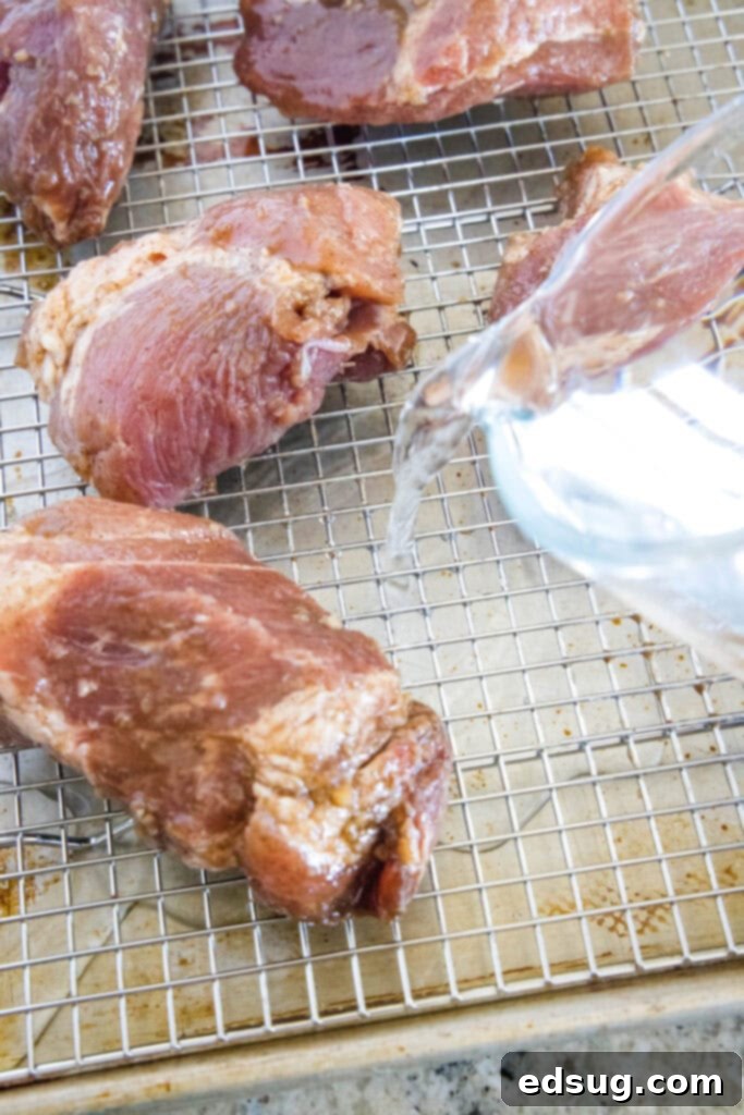 This easy char siu pork recipe is tender, juicy, and loaded with your favorite Chinese flavors like hoisin and five-spice powder.  A hand pouring water onto a baking sheet that has pieces of uncooked pork on it