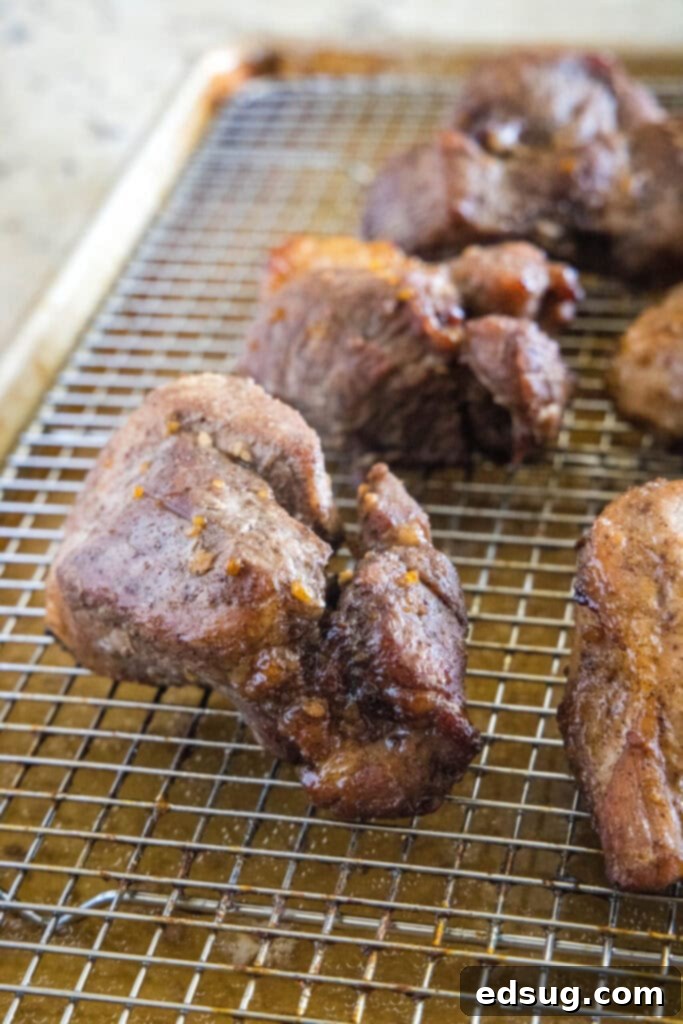 This easy char siu pork recipe is tender, juicy, and loaded with your favorite Chinese flavors like hoisin and five-spice powder.  Close up of char siu pork pieces on a wire rack on a baking sheet