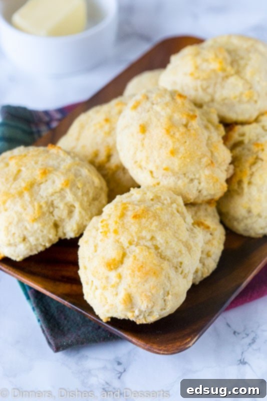 A wooden tray full of golden-brown, fluffy easy drop biscuits, with a bowl of melted butter ready for brushing in the background.