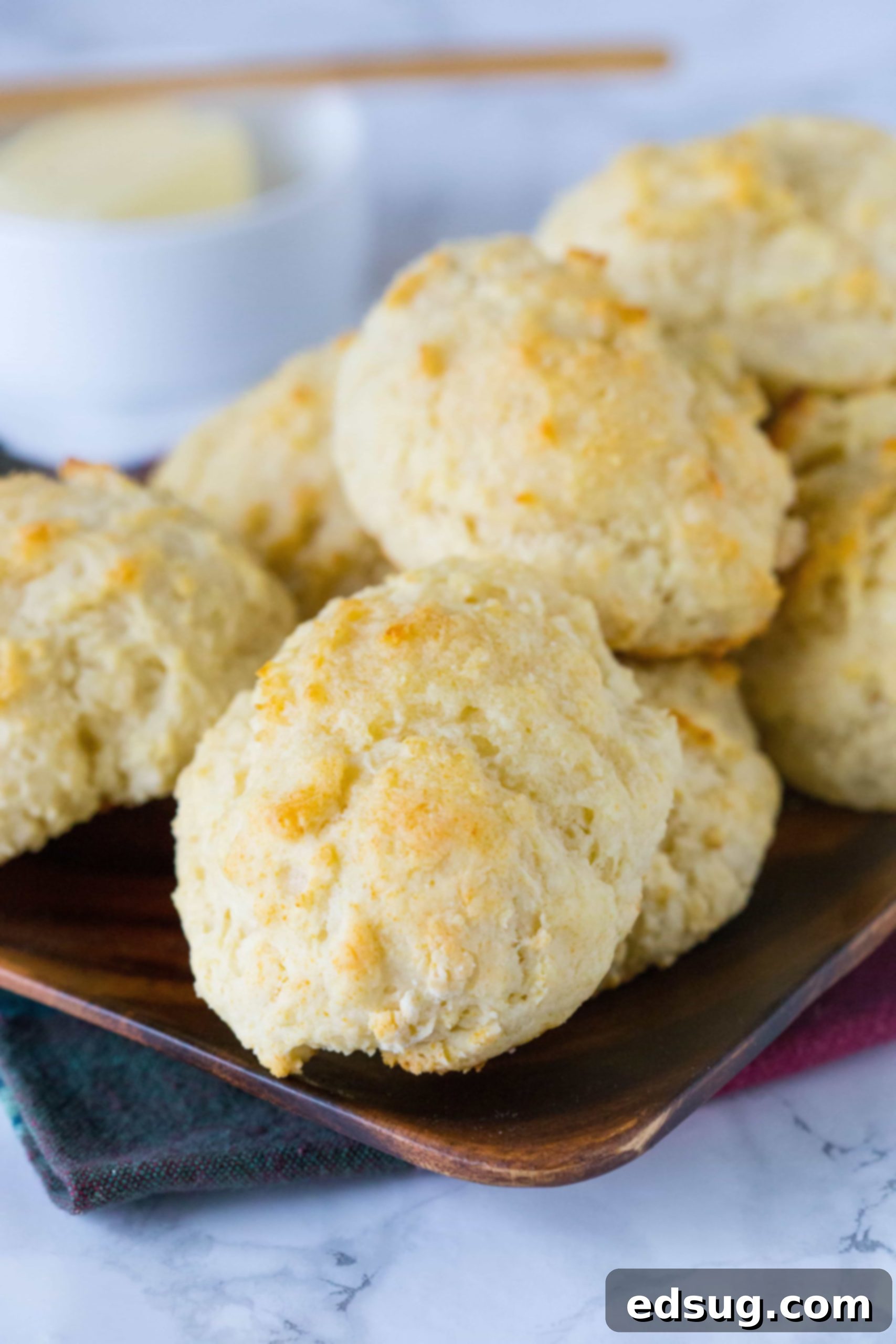 A charming wooden serving tray generously filled with freshly baked, golden-brown drop biscuits, inviting you to reach for one.