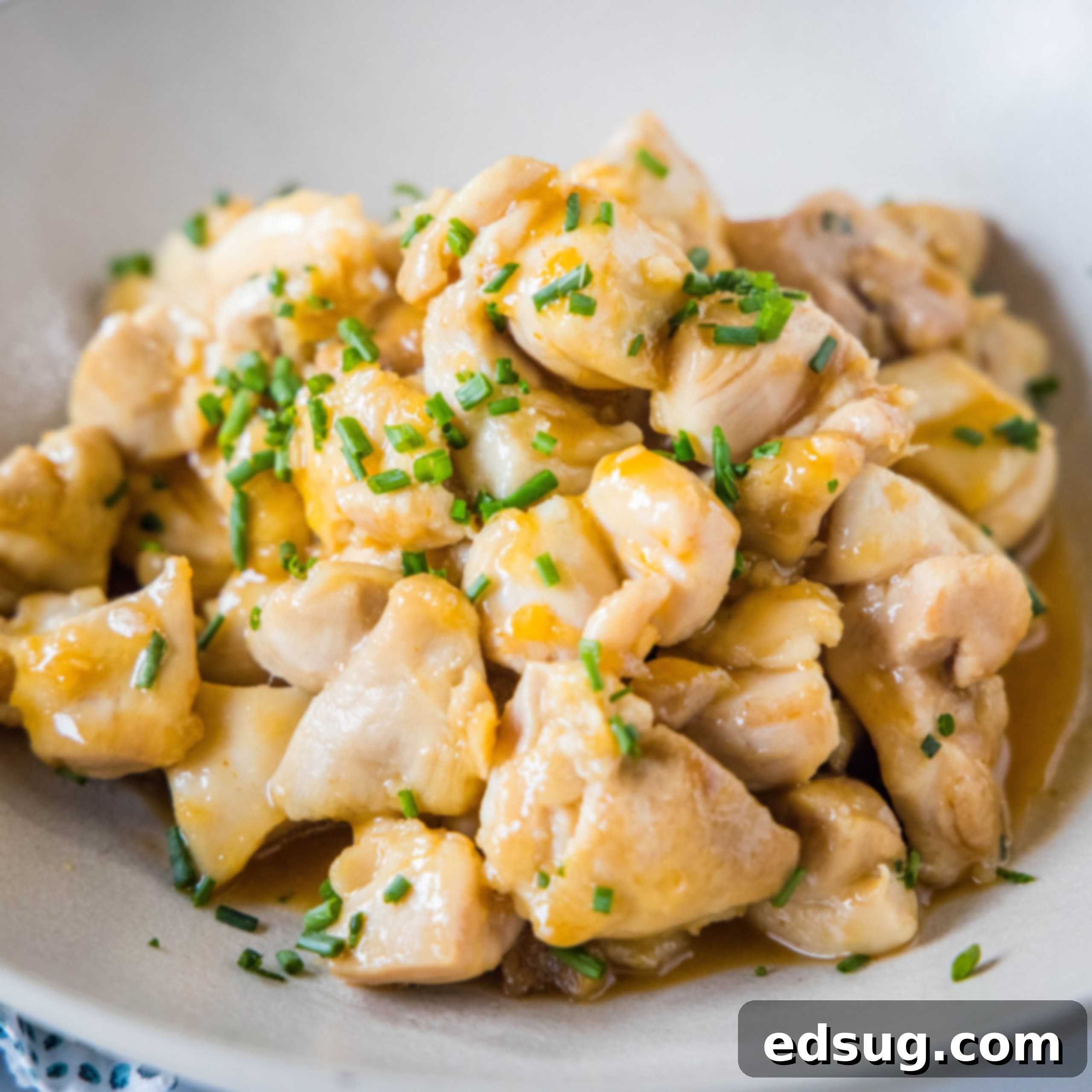 Close-up of golden brown Honey Sriracha Chicken Bites in a white bowl, garnished with green onions.