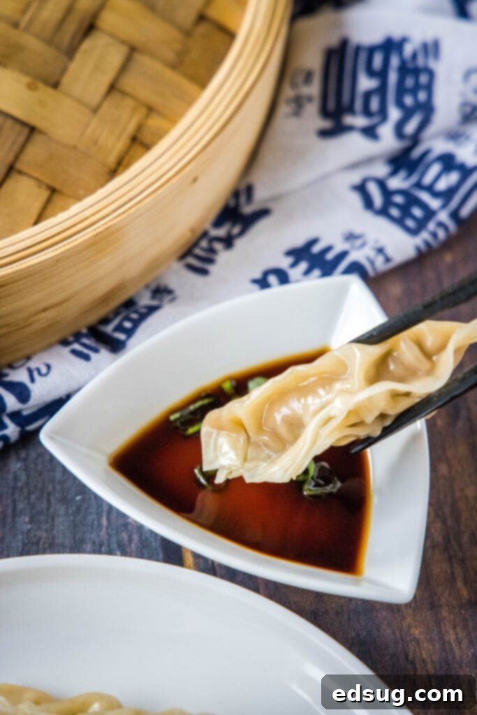 A close-up shot of a steamed pork dumpling being dipped into a small bowl of savory dipping sauce, highlighting its juicy texture.