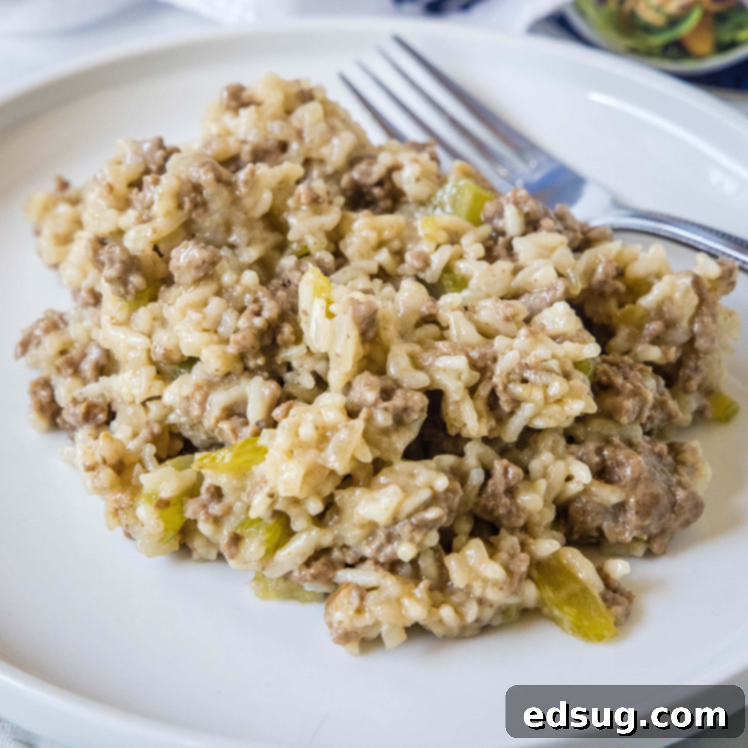 A serving of hamburger rice casserole next to a fork on a white plate.