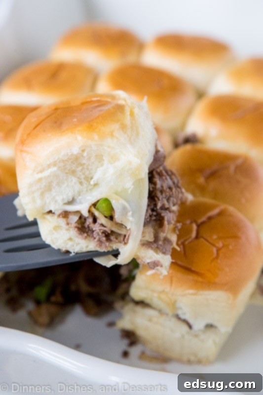 Philly Cheesesteak Sliders - little cheesesteak sliders are stuffed with sauteed onions, peppers, mushrooms, and lots of melty cheese! Great for a party, game day, or a fun and easy dinner! Close-up of baked Philly Cheesesteak sliders, showcasing the golden-brown buns and abundant melted Provolone cheese spilling out.