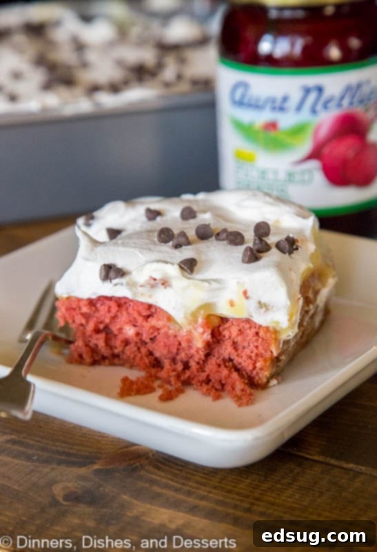 Luscious Red Velvet Poke Cake 3 A close-up of a generous slice of Beet Red Velvet Poke Cake on a white plate, highlighting the airy whipped cream, the rich vanilla pudding, and the deeply colored, moist cake layers beneath.