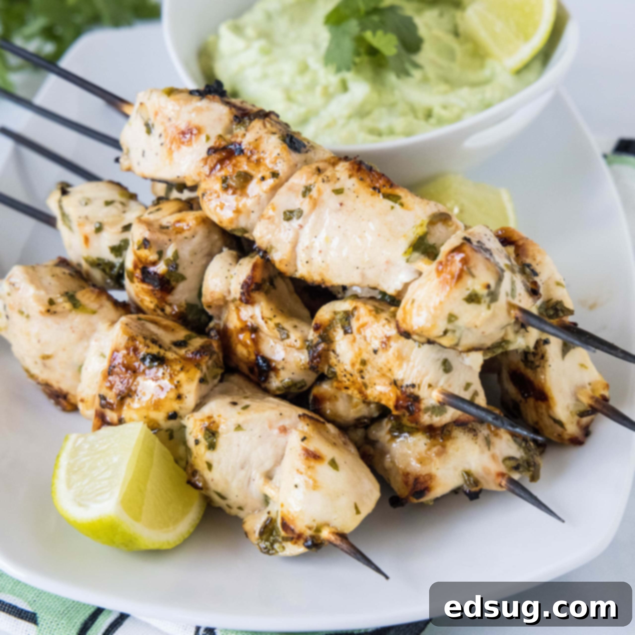 Cluck-Worthy Chicken Meals 21 A plate of grilled cilantro lime chicken skewers next to a lime wedge, with a bowl of avocado dipping sauce in the background.