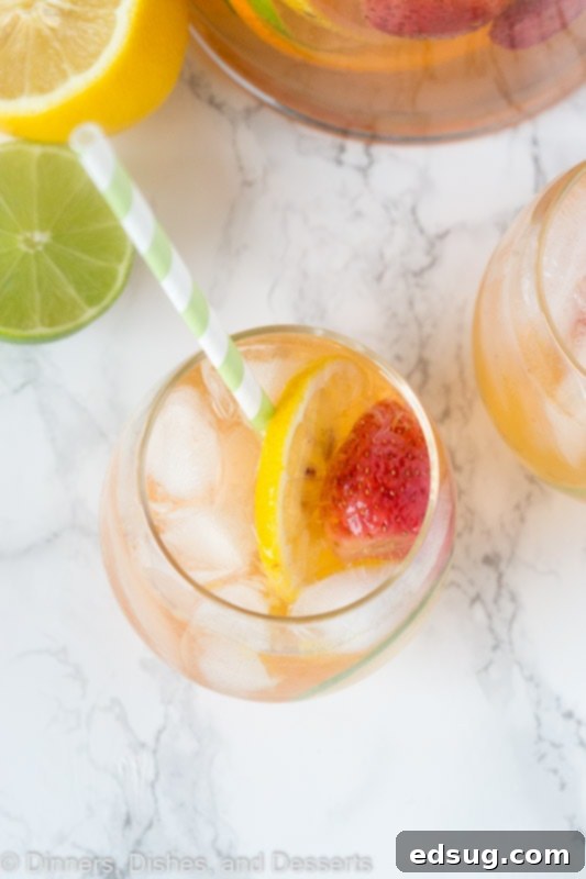 Overhead view of a glass pitcher filled with white sangria, fruit slices, and ice, ready to be served.