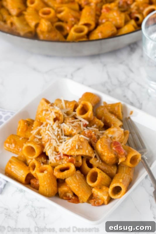 Bruschetta Chicken Pasta - an easy chicken and pasta loaded with lots of juicy tomatoes, perfectly seasoned chicken, and a flavorful pesto sauce, topped with Parmesan cheese. Quick to make for any night of the week. A large skillet filled with Bruschetta Chicken Pasta, showing the cooked pasta, chicken, and tomato-pesto sauce being mixed together before serving.