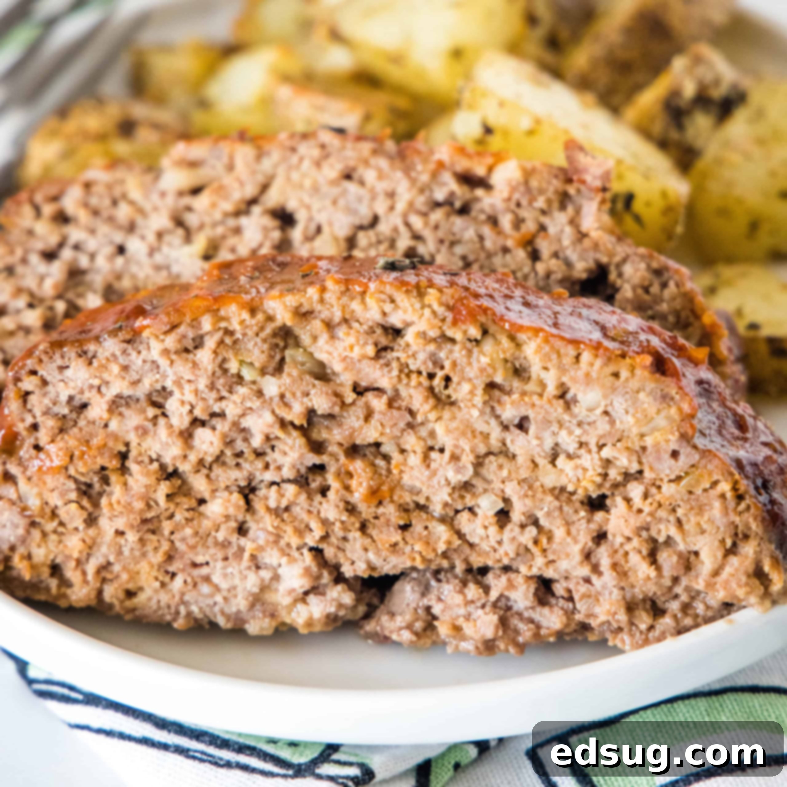 Onion soup meatloaf slices on a plate with roasted potatoes in the background.