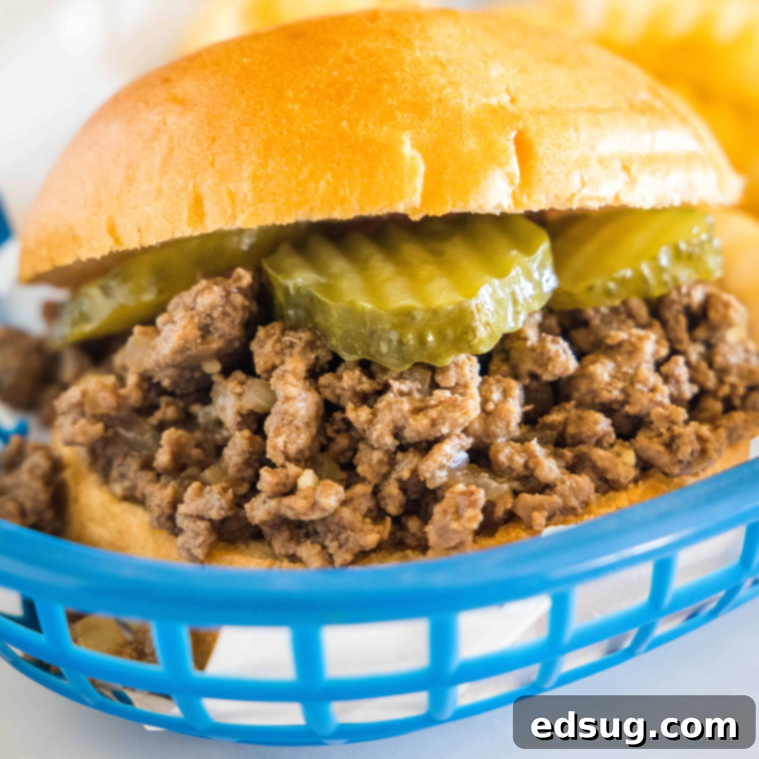 Close up of a Maid Rite loose meat sandwich garnished with pickles in a blue plastic serving basket.
