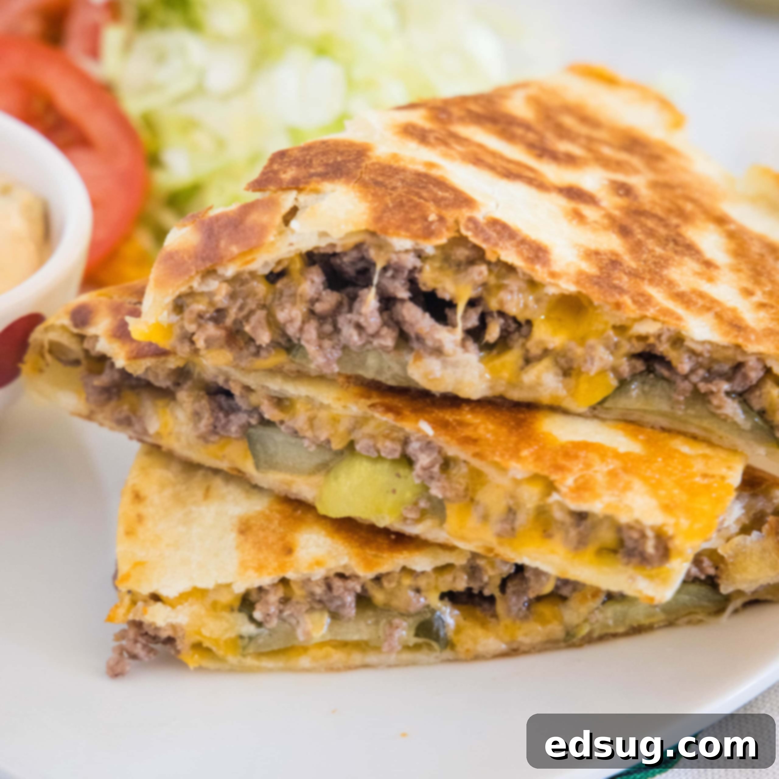 Three slices of cheeseburger quesadilla stacked on a plate.