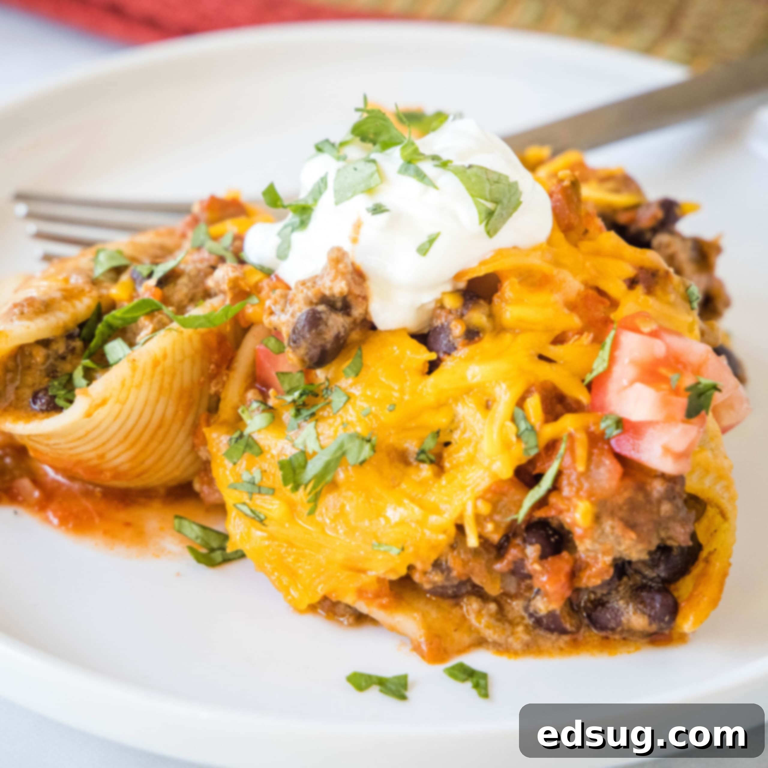 A serving of taco stuffed shells on a white plate next to a fork.
