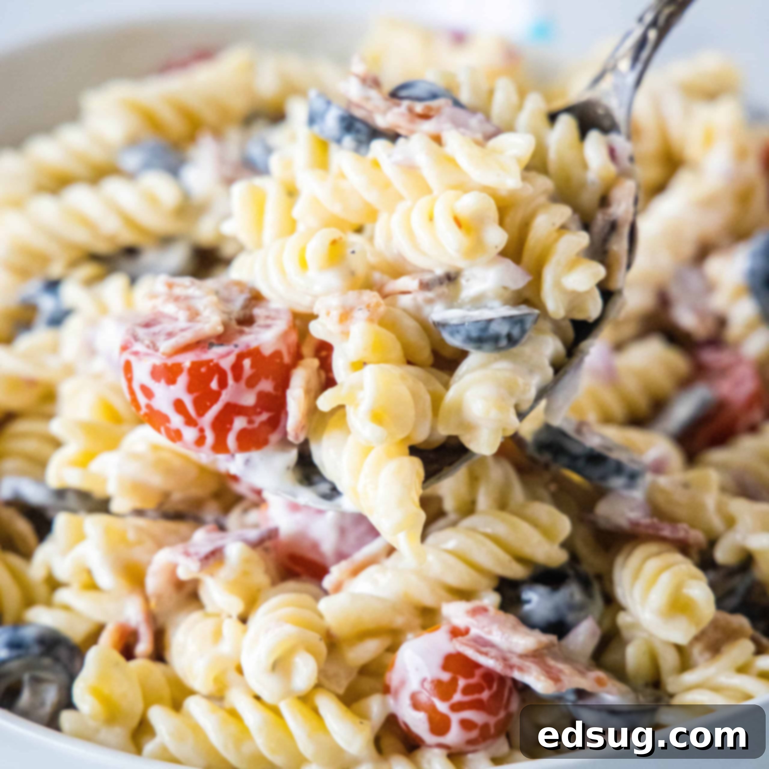 A large serving spoon scooping ranch pasta salad from a white bowl.