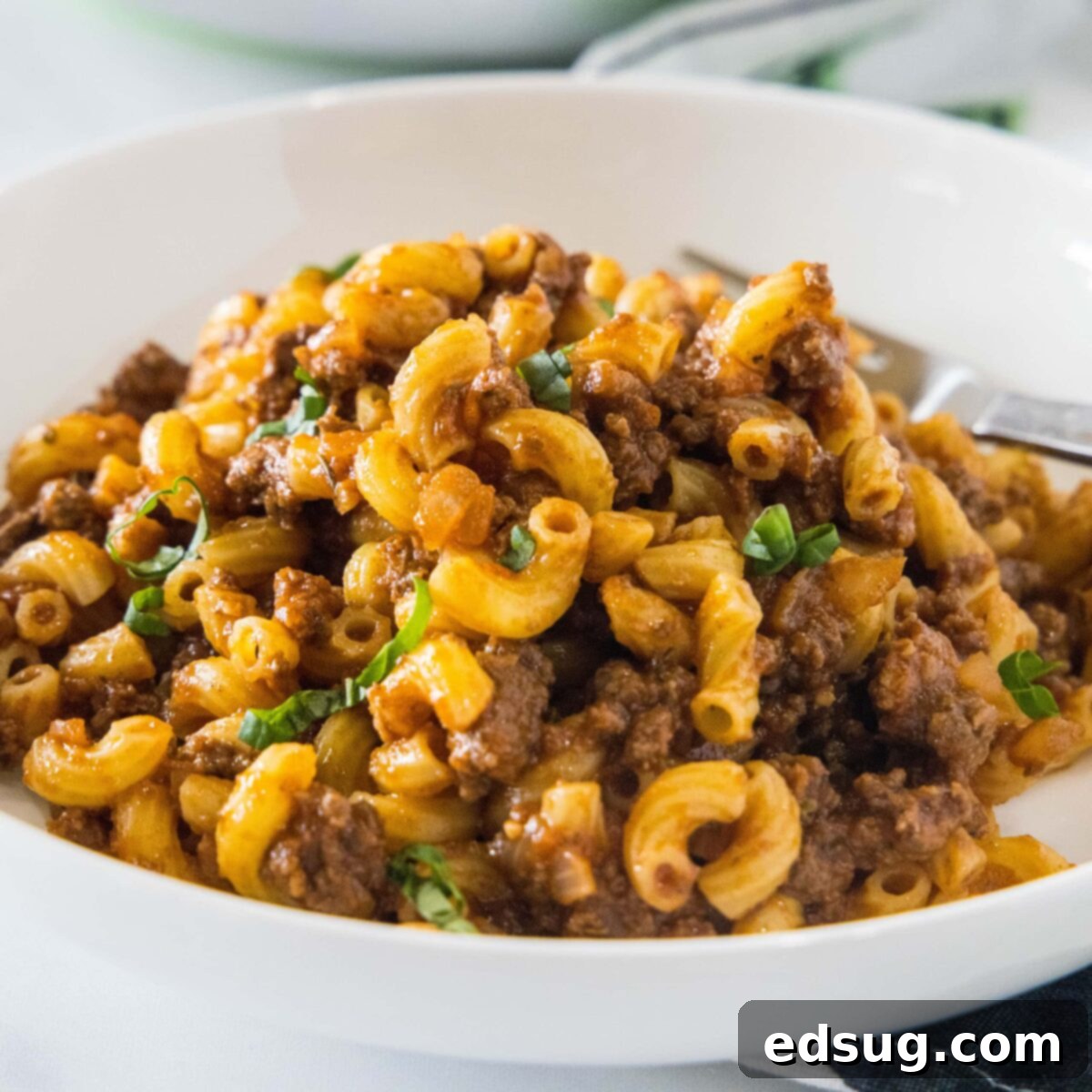 A white bowl with beefaroni and a fork