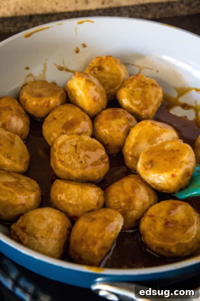 Cooked chicken meatballs being tossed in a skillet with the glossy Kung Pao sauce