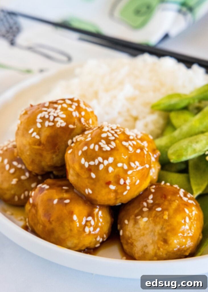 A plate of Kung Pao chicken meatballs served with white rice, garnished with sesame seeds and green onions