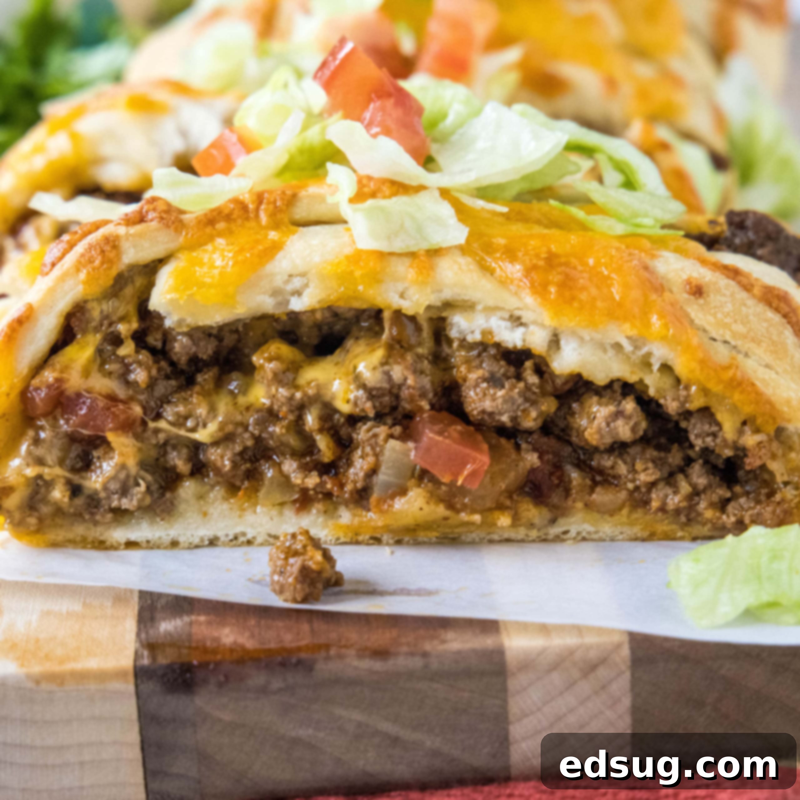 Close up of a taco braid slice filled with ground beef and topped with melted cheese, shredded lettuce, and diced tomatoes, ready to serve.