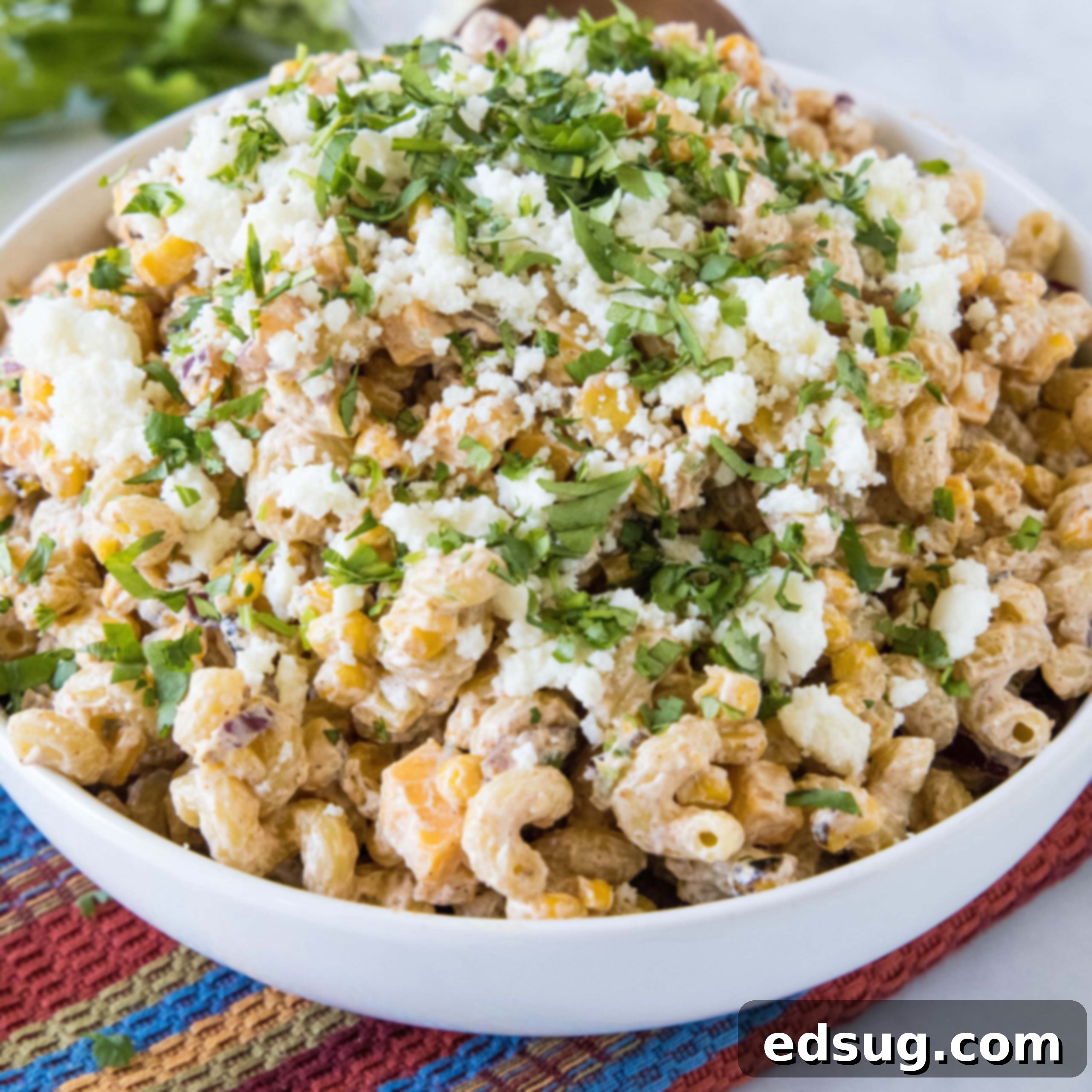A delightful bowl of Mexican street corn pasta salad, garnished with crumbled Cotija cheese and fresh cilantro.