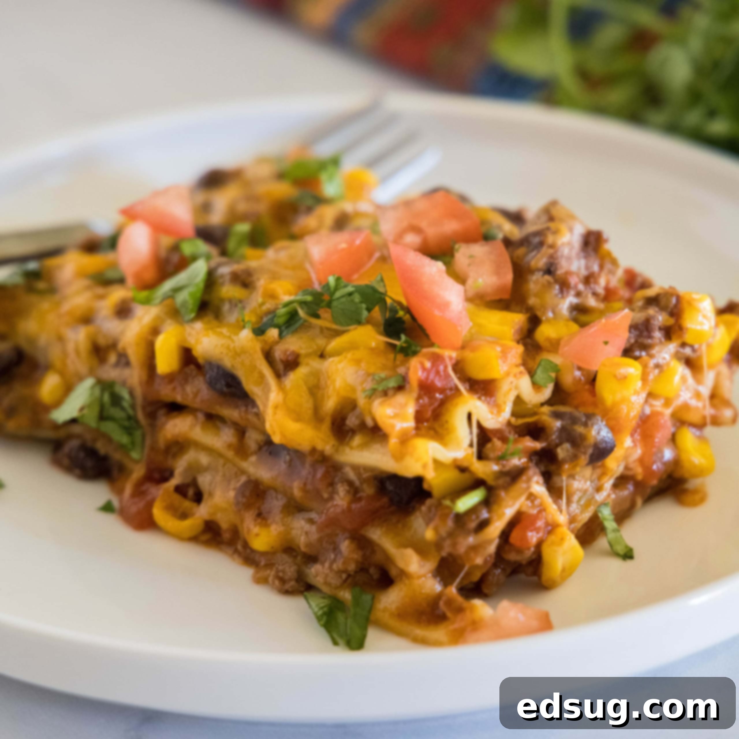 A generous serving of Mexican lasagna on a white plate, with a fork resting in the background, ready to be enjoyed.