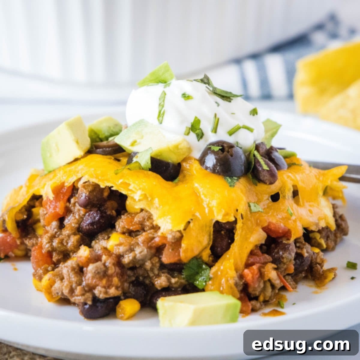 A delicious serving of taco casserole on a plate, beautifully garnished with sour cream, fresh avocado, vibrant cilantro, and black olives.