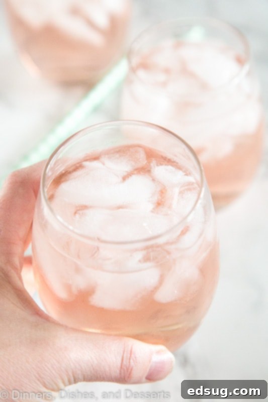 A refreshing glass of rosé wine spritzer with ice and a lemon slice.