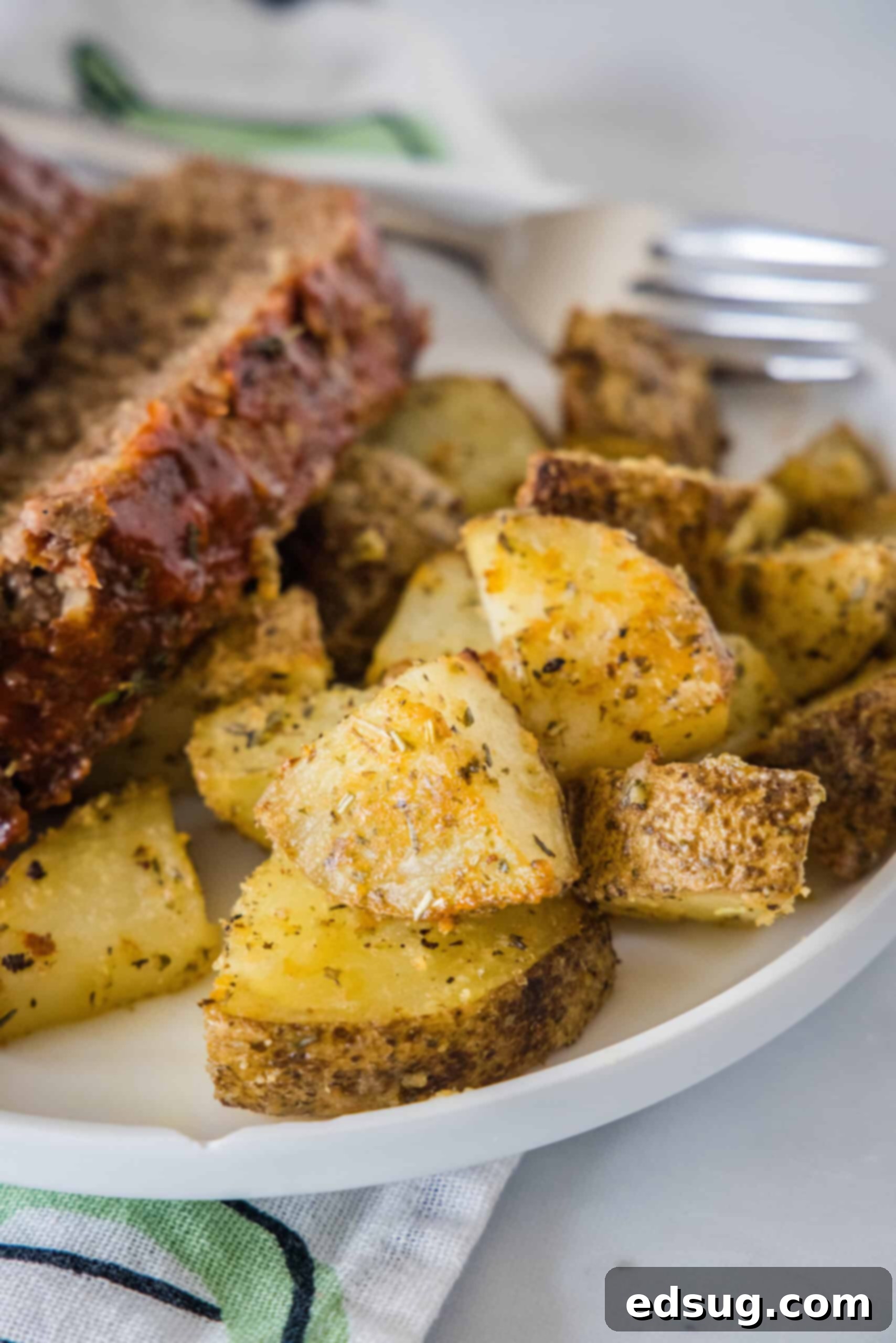 Make perfectly golden, crispy oven roasted potatoes as an easy side dish or appetizer! All it takes is olive oil and a handful of spices. Close up of seasoned oven roasted potatoes on a plate, garnished with fresh herbs.