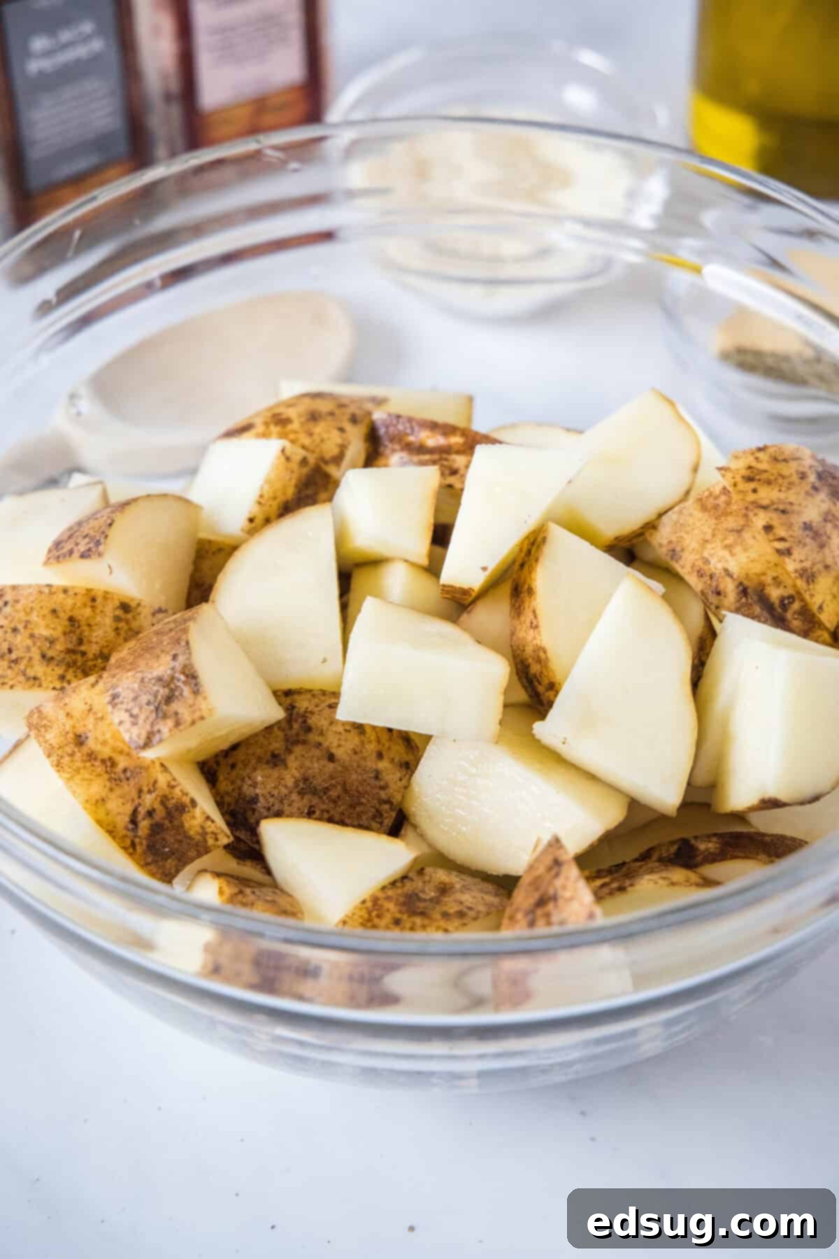 Make perfectly golden, crispy oven roasted potatoes as an easy side dish or appetizer! All it takes is olive oil and a handful of spices. Cubed potatoes in a glass bowl, ready for seasoning.