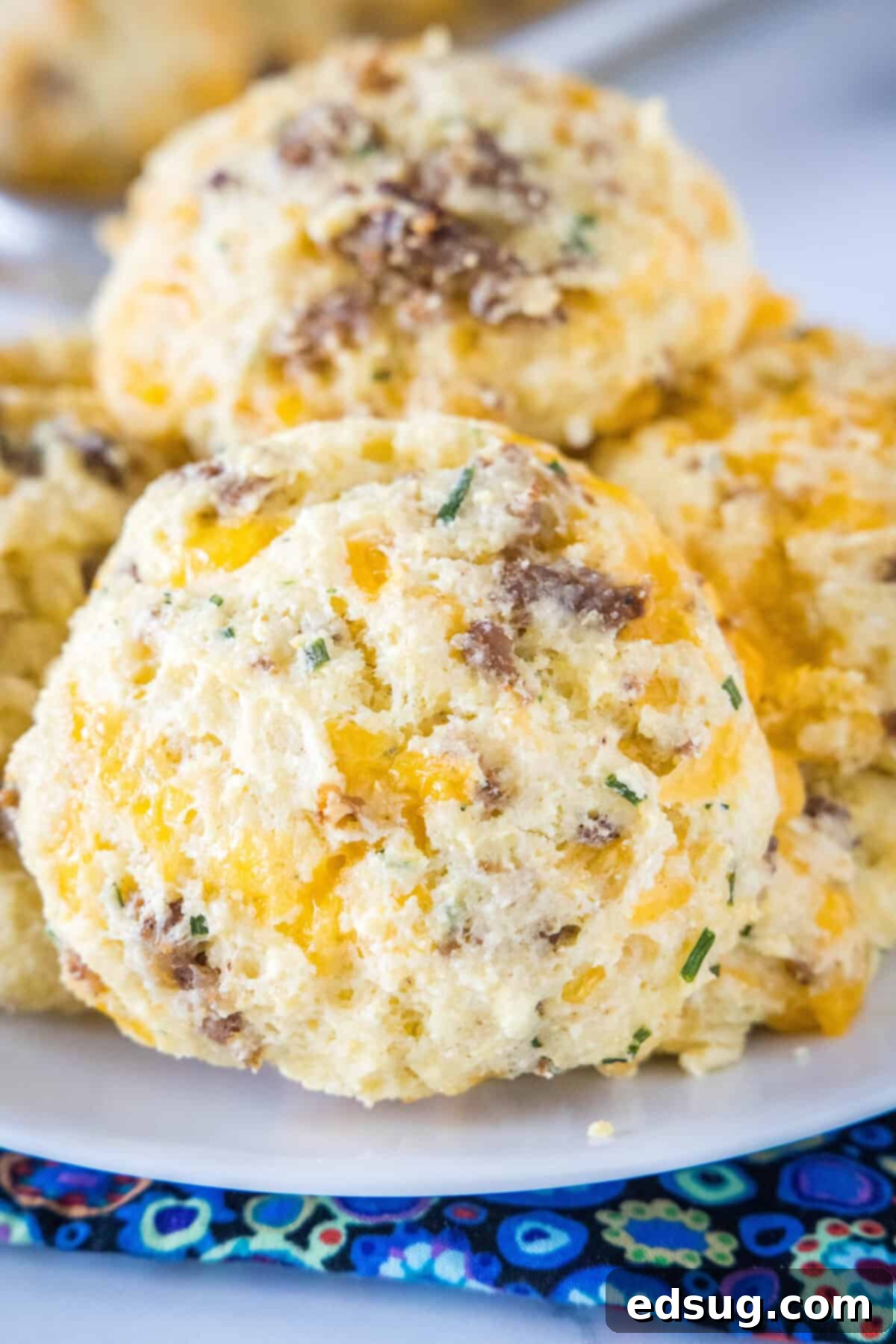 Homemade Cheese and Sausage Biscuits - light, fluffy, and packed with cheddar and savory sausage for a perfect meal. Golden-brown cheese and sausage biscuits on a white plate, ready to be served for breakfast or brunch, showcasing their fluffy texture.