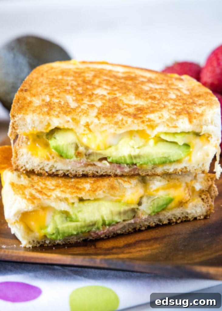 Avocado grilled cheese sandwich cut in half and stacked on a plate, showcasing melted cheese and fresh avocado slices.