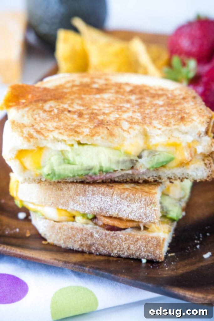 Avocado grilled cheese sandwich cut in half, revealing the layers of avocado and melted cheese, served on a plate.