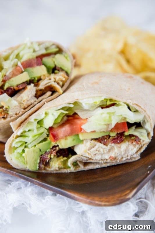 A beautifully assembled Chicken Club Wrap, showcasing layers of chicken, bacon, lettuce, tomato, and avocado nestled within a flour tortilla.