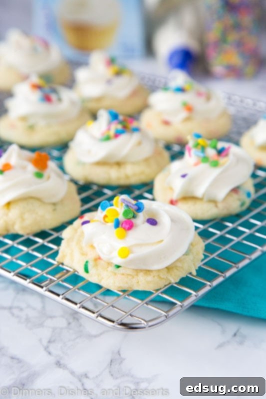 Sparkle-Topped Funfetti Cake Mix Cookies 2 A close-up view of freshly baked Frosted Funfetti Cake Mix Cookies cooling on a wire rack, adorned with creamy vanilla frosting and colorful sprinkles, ready to be enjoyed.