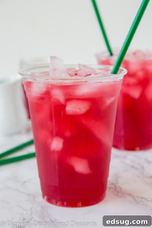 A tall glass of vibrant pink Passion Tea Lemonade with ice and lemon slices