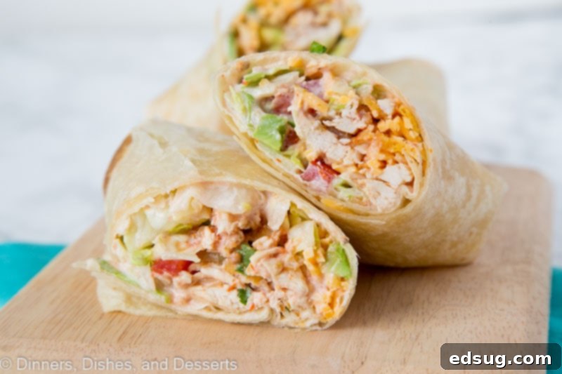 A chicken wrap cut in half diagonally, with one half resting on top of the other, with another wrap in the background