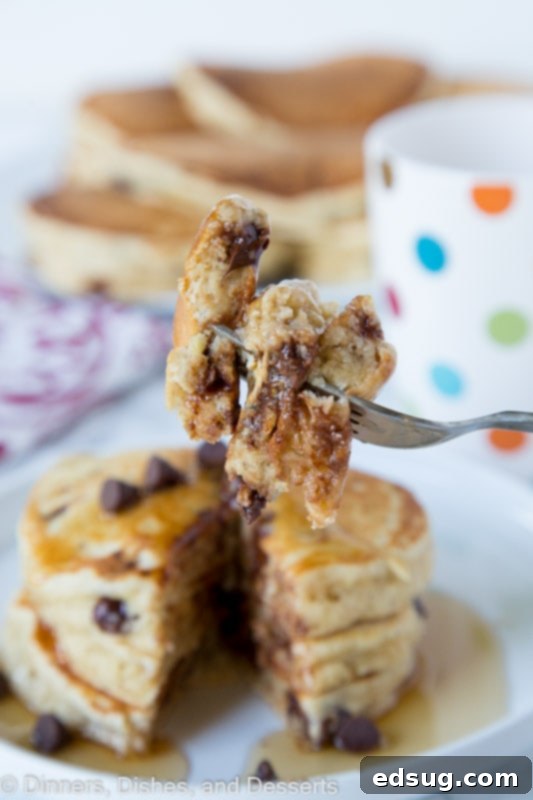Close-up of fluffy banana pancakes with melted chocolate chips, one with a bite taken out by a fork.